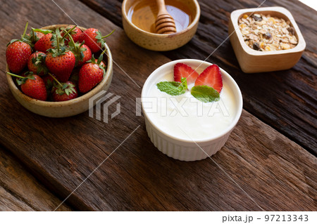Strawberry yogurt in a wooden bowl with granola, honey, mint and fresh strawberry on wooden background. Health food concept.. Strawberry yogurt in a wooden bowl with granola, honey, mint and fresh strawberry on wooden background. Health food concept.. 97213343