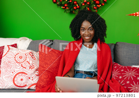 Beautiful african woman working with laptop on couch at home on Christmas Eve Beautiful african woman working with laptop on couch at home on Christmas Eve 97213801