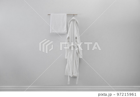 Rack with clean bathrobe and towel on light wall 97215961