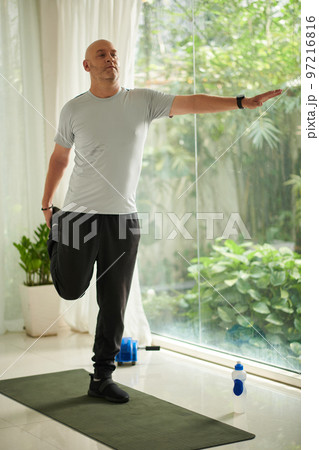 Mature man balancing on one leg when working out at home in the morning 97216816