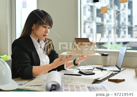 Beautiful architects woman working on design of a construction plan and scale model house at office Beautiful architects woman working on design of a construction plan and scale model house at office 97219545
