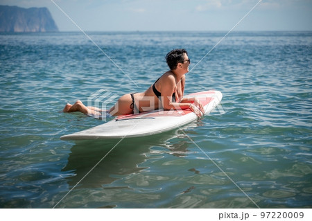 Woman sap sea. Sports girl on a surfboard in the sea on a sunny summer day. In a black bathing suit, he lies on a sap in the sea. Rest on the sea. Woman sap sea. Sports girl on a surfboard in the sea on a sunny summer day. In a black bathing suit, he lies on a sap in the sea. Rest on the sea. 97220009