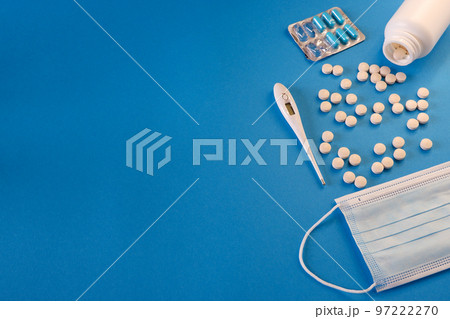 Medicine and health concept. Blister with capsules, pills, thermometer and medical mask on a blue background. Place for your text. 97222270