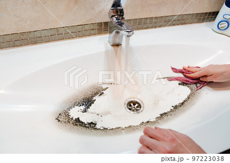 a woman washes the sink with wet rag in the bathroom. 97223038