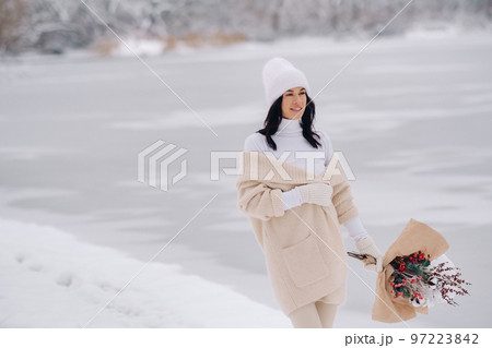 A girl in a beige cardigan and winter flowers walks in nature in the snowy season. Winter weather 97223842
