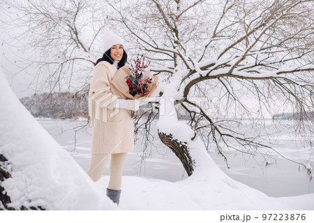 A girl in a beige cardigan and winter flowers walks in nature in the snowy season. Winter weather 97223876