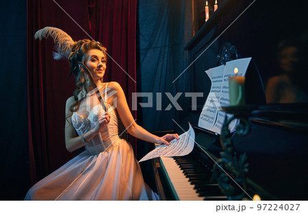 Inspiration. Portrait of beautiful young woman in image of medieval person, princess sitting at the piano in tender white dress and playing. Comparison of eras, beauty, history, art Inspiration. Portrait of beautiful young woman in image of medieval person, princess sitting at the piano in tender white dress and playing. Comparison of eras, beauty, history, art 97224027
