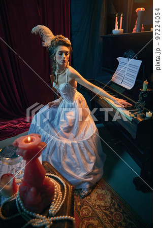 Young tender girl in image of medieval princess in elegant white dress sitting at the piano. Learning music composition. Comparison of eras, beauty, history, art Young tender girl in image of medieval princess in elegant white dress sitting at the piano. Learning music composition. Comparison of eras, beauty, history, art 97224054