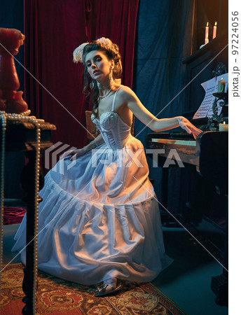 Portrait of young attractive girl in image of medieval person, in elegant white dress sitting at the piano and playing. Comparison of eras, beauty, history, art, Portrait of young attractive girl in image of medieval person, in elegant white dress sitting at the piano and playing. Comparison of eras, beauty, history, art, 97224056