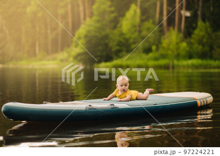 The child lies floating on the water on a large sup board. Water sports 97224221