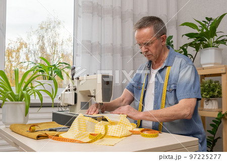 Senior man seamstress sitting and sews on sewing machine in studio. 97225277