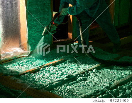 Male builder insulating wooden frame house. Cropped view of man worker spraying polyurethane foam on floor inside of future cottage, using plural component gun. Construction and insulation concept. Male builder insulating wooden frame house. Cropped view of man worker spraying polyurethane foam on floor inside of future cottage, using plural component gun. Construction and insulation concept. 97225409