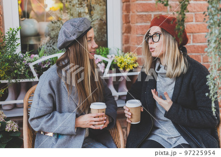 Young female best friends talking to each other discussing interesting themes during free time hipster girls joking and having fun together enjoying recreation with coffee to go on urban background Young female best friends talking to each other discussing interesting themes during free time hipster girls joking and having fun together enjoying recreation with coffee to go on urban background 97225954