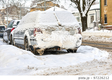 Riga, Latvia - 13 December, 2022: Frozen car covered with snow layer in winter day parked on the street of city. 97226212