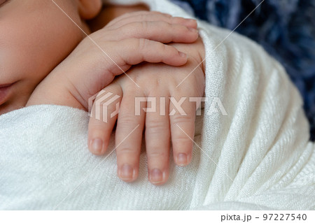 Close-up of little baby handles. The sleeping Newborn boy under a white knitted blanket lies on the blue fur. 97227540