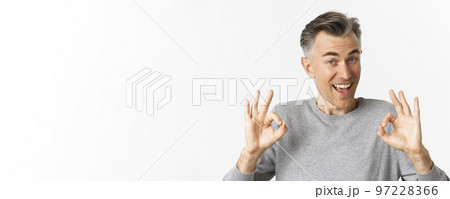 Close-up of handsome middle-aged man, showing okay signs and looking amazed, recommending something cool, standing over white background 97228366