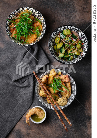 Three bowls of appetizer on dark background. Kimchi cabbage salad, Smashed Cucumber salad, Japanese prawns and vegetable tempura. Asian cuisine Three bowls of appetizer on dark background. Kimchi cabbage salad, Smashed Cucumber salad, Japanese prawns and vegetable tempura. Asian cuisine 97228555