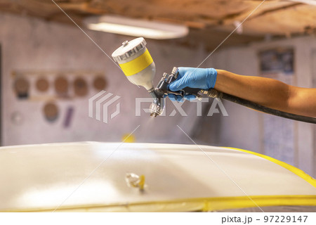 Man with protective clothes and mask painting car using spray compressor. Selective focus. 97229147