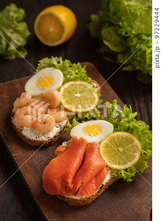 The toasts with boiled eggs, salad lettuce, lemon slime, shrimps and smoked salmon. 97229444