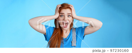 Shocked redhead girl shouting panic, feel pressured deadlines, scared see mess, grab head, scream frightened distressed, stare camera hopeless, anxiously react losing lottery, blue background 97230160