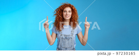 Motivated happy cheerful redhead silly curly woman pointing up inrdex finger smiling charmed impressed excited showing awesome promo discuss interesting advertisement blue background Motivated happy cheerful redhead silly curly woman pointing up inrdex finger smiling charmed impressed excited showing awesome promo discuss interesting advertisement blue background 97230165