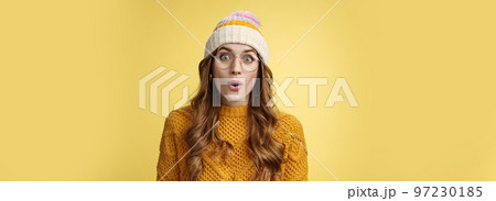 Surprised amazed charismatic good-looking young female student widen eyes wondered say wow amazed standing shocked impressed yellow background, wearing nerd glasses hat sweater 97230185