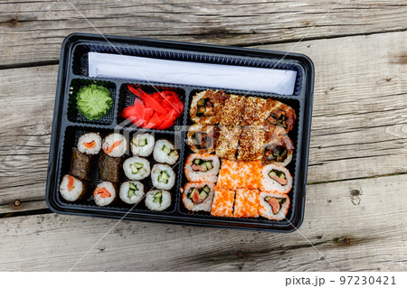 Set of sushi rolls in plastic box on wooden table. Sushi for take away or delivery of sushi in plastic container. Top view Set of sushi rolls in plastic box on wooden table. Sushi for take away or delivery of sushi in plastic container. Top view 97230421