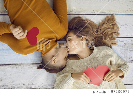 Young couple in love are kissing lying on floor with valentine hearts in their hands. 97230975