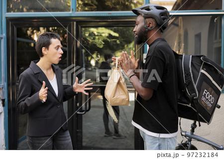 Woman shouting at office food delivery service courier, receiving wrong order, deliveryman carrying lunch late. Man giving impulsive unsatisfied customer takeaway meal near company building Woman shouting at office food delivery service courier, receiving wrong order, deliveryman carrying lunch late. Man giving impulsive unsatisfied customer takeaway meal near company building 97232184