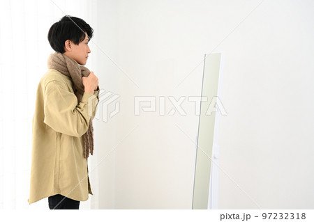 屋内で姿見を見ながらマフラーをまく若い男性 97232318
