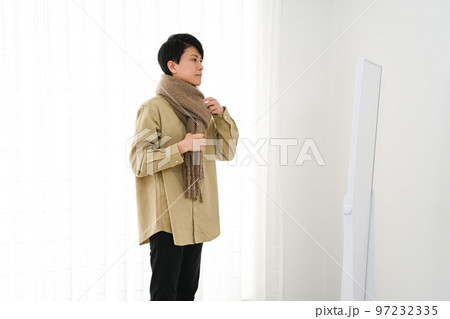 屋内で姿見を見ながらマフラーをまく若い男性 97232335