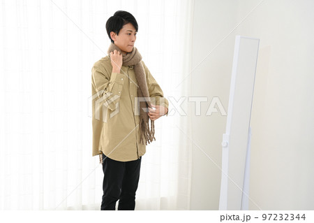 屋内で姿見を見ながらマフラーをまく若い男性 97232344