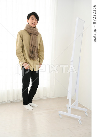 屋内で姿見を見ながらマフラーをまく若い男性 97232356
