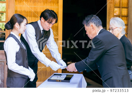 お葬式・告別式・お通夜の受付で香典を渡す高齢者の遺族・弔問客と葬祭ディレクター 97233513