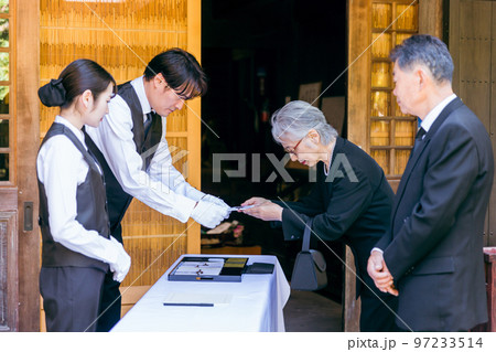 お葬式・告別式・お通夜の受付で香典を渡す高齢者の遺族・弔問客と葬祭ディレクター お葬式・告別式・お通夜の受付で香典を渡す高齢者の遺族・弔問客と葬祭ディレクター 97233514