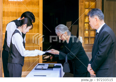 お葬式・告別式・お通夜の受付で香典を渡す高齢者の遺族・弔問客と葬祭ディレクター 97233515