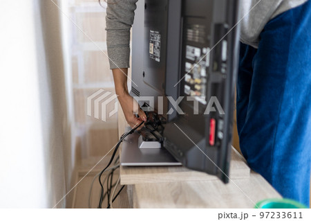 引っ越しのためテレビやレコーダーののコード類を抜こうとしている若い女性の手元 97233611