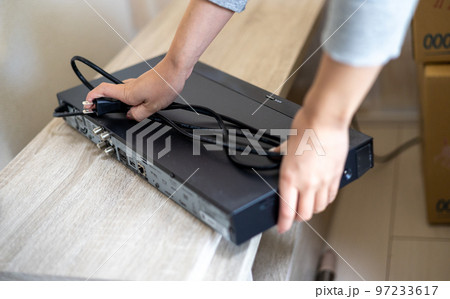 引っ越しのためテレビやレコーダーののコード類を抜こうとしている若い女性の手元 引っ越しのためテレビやレコーダーののコード類を抜こうとしている若い女性の手元 97233617