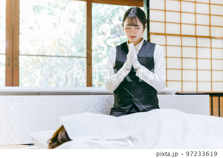 仏衣を着せる納棺師・セレモニースタッフ・葬祭ディレクター・葬儀スタッフの日本人女性（合掌） 97233619