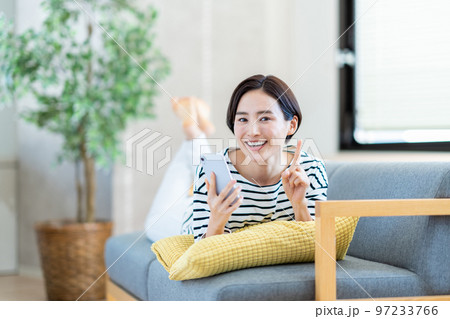 ソファーでスマートフォンを操作する女性。 ソファーでスマートフォンを操作する女性。 97233766