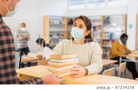 Young woman in protective mask returning books to to librarian 97234256