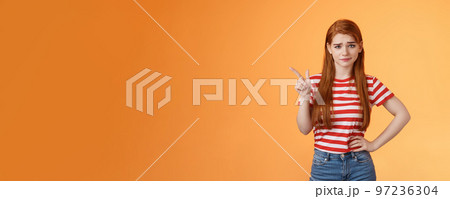 Doubtful redhead girl not buy your talks, smirking hesitant express disbelief, unimpressed about suspicious offer, pointing upper left corner wondered, stand orange background uncertain Doubtful redhead girl not buy your talks, smirking hesitant express disbelief, unimpressed about suspicious offer, pointing upper left corner wondered, stand orange background uncertain 97236304