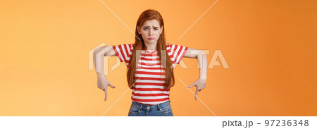 Cute timid hesitant ginger female taking tough decision feel pressured upset, frowning, pulling gloomy unhappy face, pointing down disappointed, uneasy taking decision, orange background Cute timid hesitant ginger female taking tough decision feel pressured upset, frowning, pulling gloomy unhappy face, pointing down disappointed, uneasy taking decision, orange background 97236348