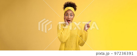 Shocked impressed emotive african-american girl afro hairstyle gasping amazed touch cheek stunned widen eyes pointing upper left corner surprised telling you unbelievable discovery yellow background 97236391