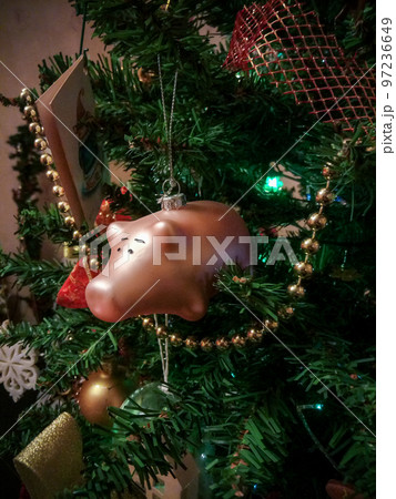 a glass toy in the form of a pink pig hangs on a decorated Christmas tree a glass toy in the form of a pink pig hangs on a decorated Christmas tree 97236649