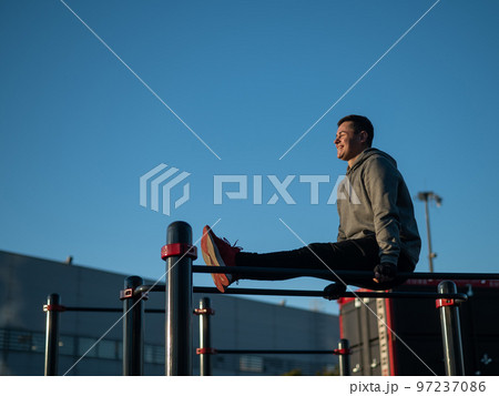 Young caucasian man doing parallel bars exercise outdoors.  97237086