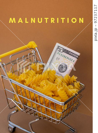MALNUTRITION text against Shopping trolley cart Filled With Pasta with 5 US dollar paper money banknote on Beige background. Food and groceries shopping price increase, Rising food cost food crisis 97237117