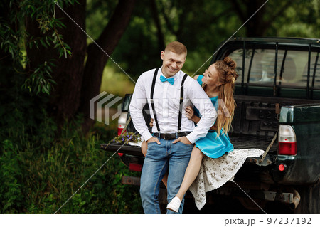 A young couple is sitting in a pickup truck trailer in the forest in summer. A young couple is sitting in a pickup truck trailer in the forest in summer. 97237192