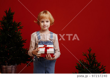 Child holding a gift box on a red background Child holding a gift box on a red background 97237240