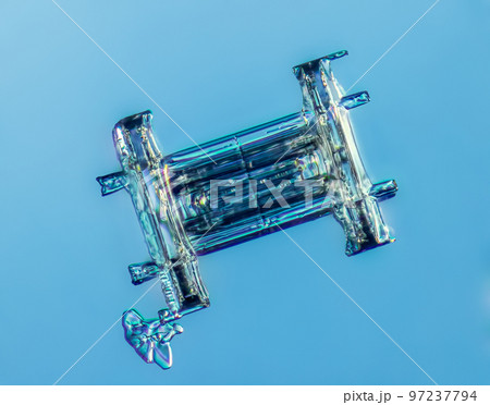 Real column snowflake at high magnification. Macro photo of small rimmed snow crystal, snowflake glowing on dark blue background Real column snowflake at high magnification. Macro photo of small rimmed snow crystal, snowflake glowing on dark blue background 97237794